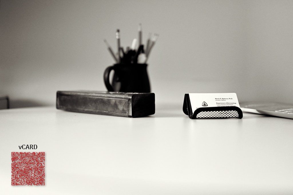Dr. Alphonse's business card in a holder on a desk, alongside a scannable vCard QR code with his contact details